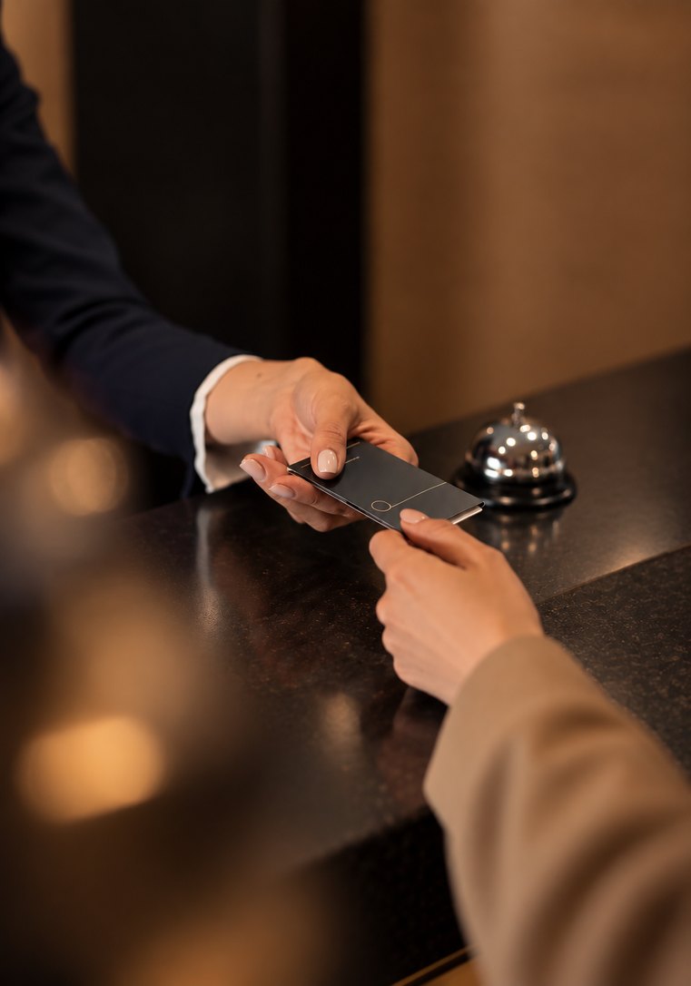 A guest holds a phone beside a hotel bell on the reception desk.